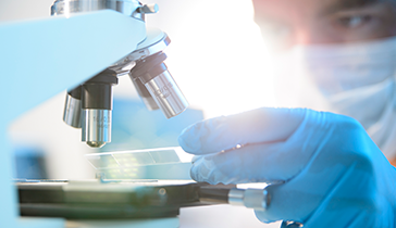 Researcher looking at substance underneath a microscope 